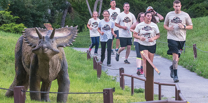 Runners on trail near a model triceratops