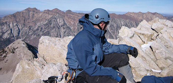 man in climbing gear at mountain peak in winter clothing